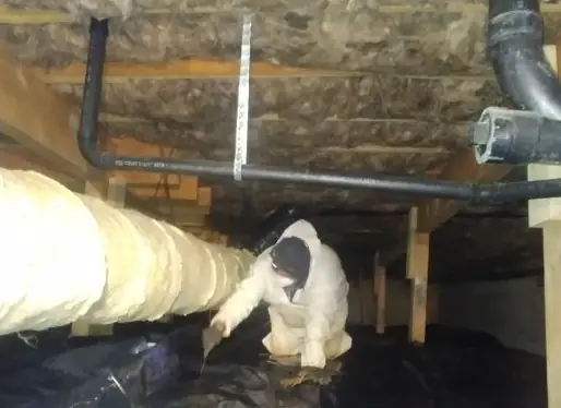 RGS crew member in a respirator working in a tight crawl space beside insulated ductwork and black vapor barrier